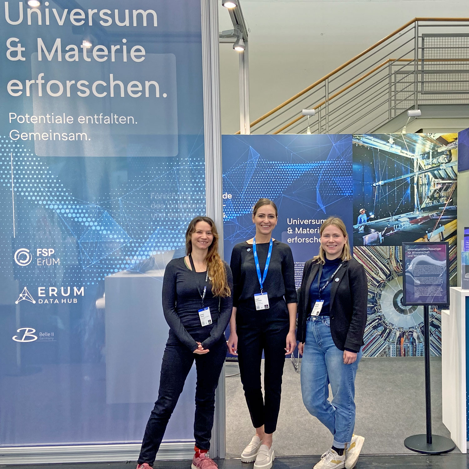 Foto © Peter Fackeldey | ErUM-Data-Hub Drei Frauen stehen vor dem Gemeinschaftsstand des LHC-ErUM-FSP-Büros